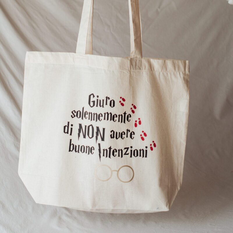 Tote bag color beige con la scritta "Giuro solennemente di non avere buone intenzioni" con il font di Harry Potter in nero, cinque impronte rosse di scarpa in sequenza e il disegno degli occhiali di Harry Potter color dorato.